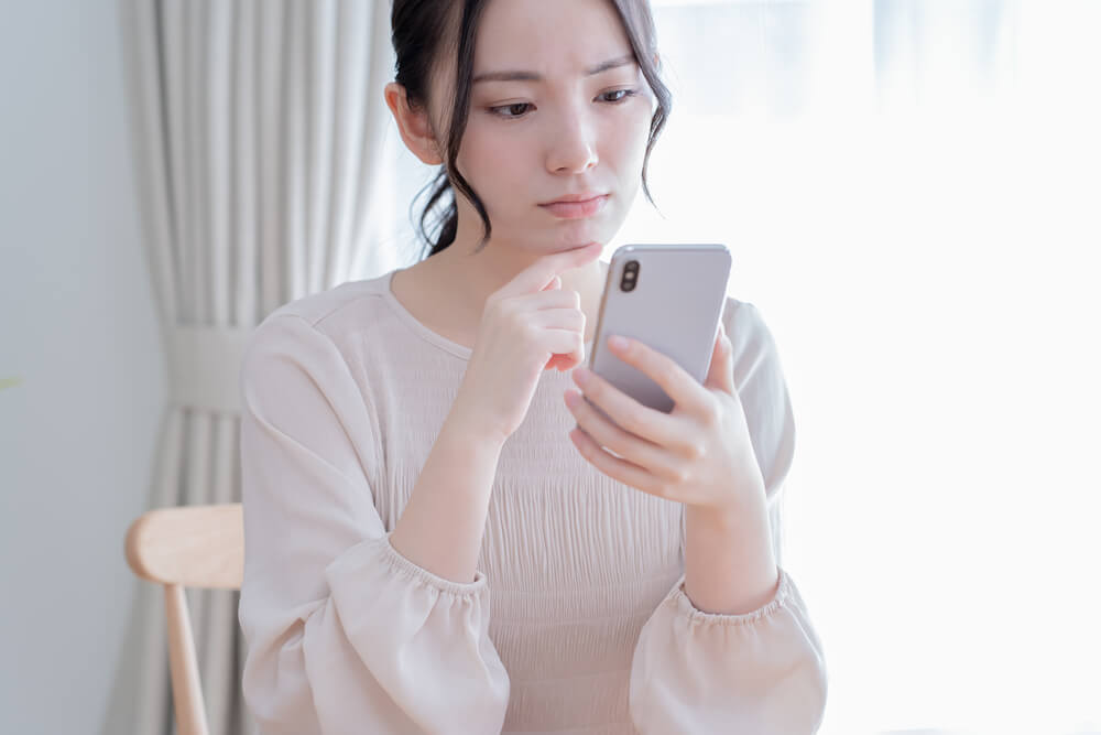 スマホを見ながら悩む女性