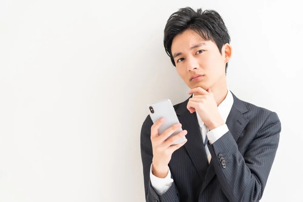 スマホを持ちながら考える男性